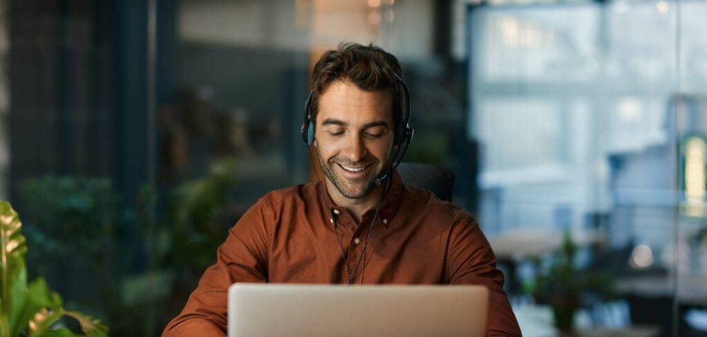 Businessman smiling and talking with a client over a headset while working alone at his desk in a dark office after hours